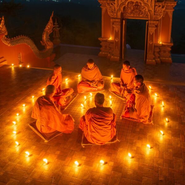 Group of young and senior monk sit in a circle with several lighting candle surround