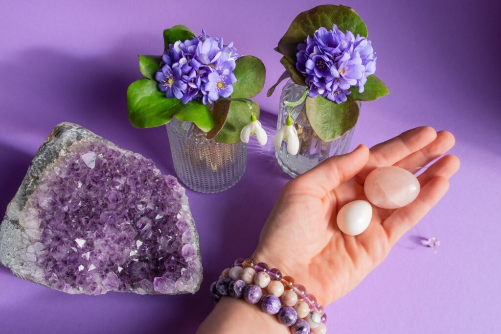 Woman hand in stone bracelets on purple background holding two yoni eggs -rose quartz and white jade